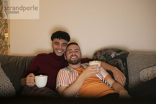 Glücklich liebevoll Homosexuell männliches Paar mit heißem Kakao vor dem Fernseher auf dem Sofa