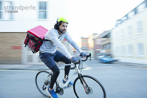 Männlicher Fahrradkurier  der in einem städtischen Viertel Lebensmittel auf dem Fahrrad ausliefert