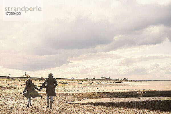 Paar hält Hände zu Fuß auf sonnigen ruhigen Winter Strand