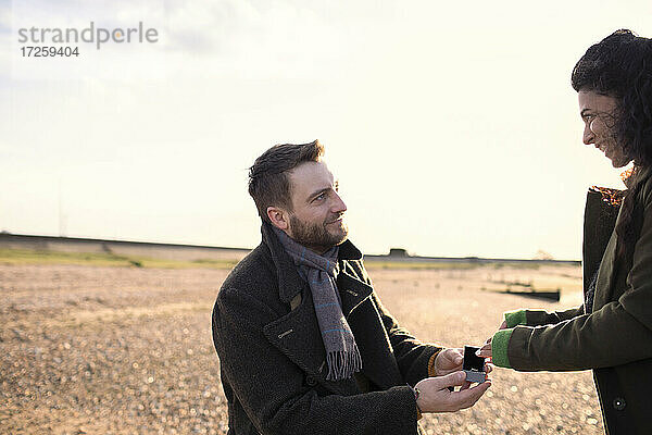 Mann macht seiner Freundin am sonnigen Winterstrand einen Heiratsantrag