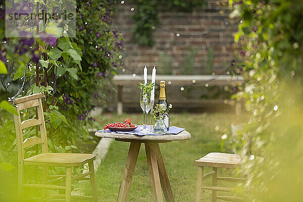 Champagner und rote Johannisbeeren auf idyllischem Gartentisch mit Kerzen