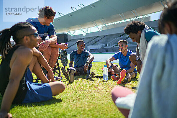 Junge männliche Sportler Freunde ausruhen und reden auf sonnigen Stadion Rasen