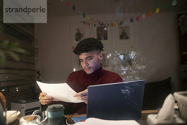 Konzentrierter junger Mann mit Papierkram arbeitet spät im Home Office
