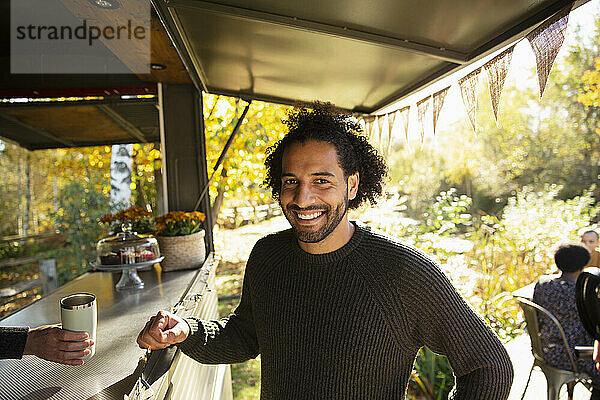 Porträt glücklicher männlicher Kunde  der Kaffee an einem Essenswagen im Park bestellt