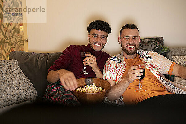 Glückliche Homosexuell männliches Paar mit Wein und Popcorn beobachten Film auf dem Sofa