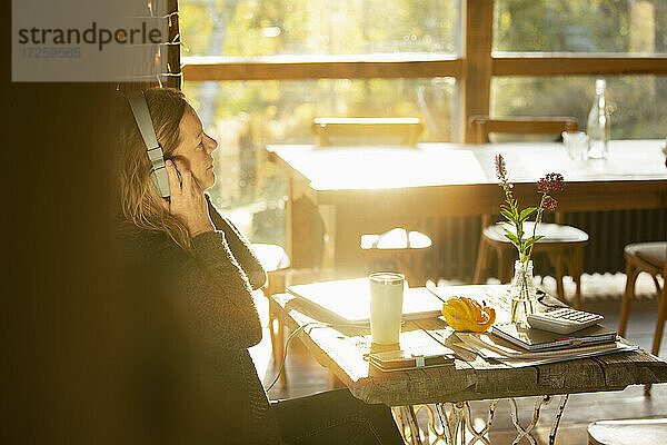 Geschäftsfrau mit Kopfhörer arbeiten in sonnigen Café