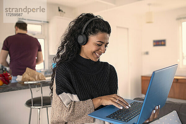 Glückliche Frau mit Kopfhörer arbeiten von zu Hause aus am Laptop