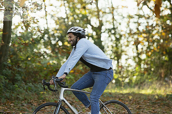 Glücklicher junger Mann fährt Fahrrad im Herbst Park