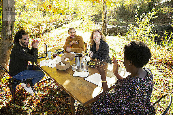 Glückliche Geschäftsleute essen und arbeiten am Tisch im sonnigen Herbst Park