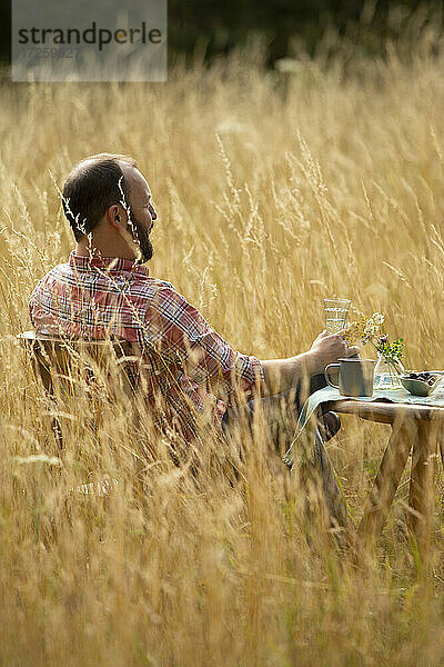 Mann entspannt am Tisch im sonnigen Sommer hohes Gras