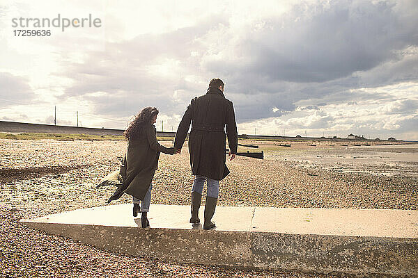 Paar in Wintermäntel halten Hände zu Fuß auf sonnigen Strand