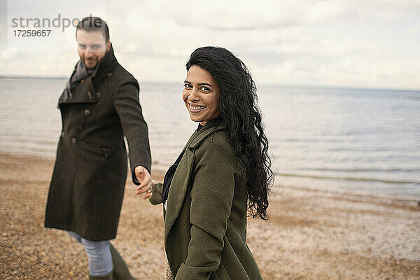 Porträt glückliches Paar in Wintermänteln halten Hände auf Ozean Strand