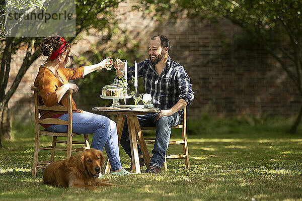 Glückliches Paar mit Hund Toasting Gläser am Tisch im Sommer Garten