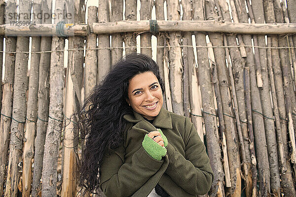 Portrait glückliche schöne Frau im Wintermantel am Holzzaun