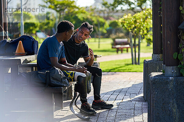 Trainer und junger männlicher amputierter Sportler im Gespräch auf einer Parkbank