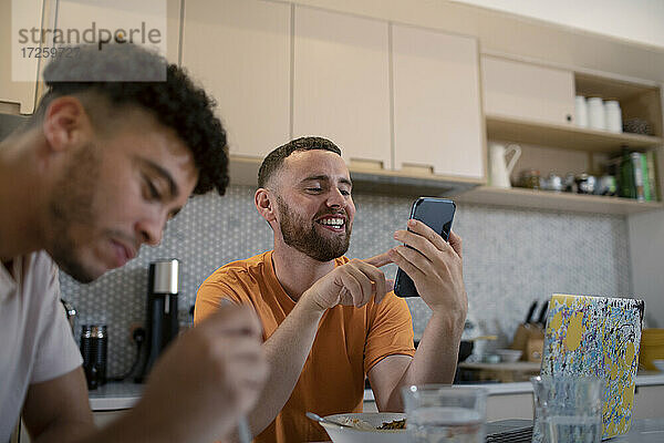 Glückliche Homosexuell männliches Paar mit Smartphone und Essen in der Küche