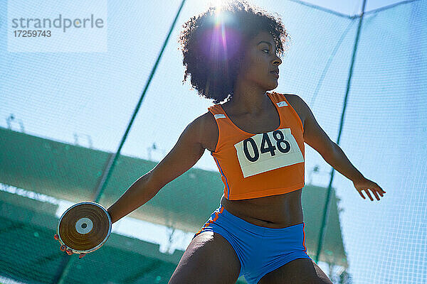 Weibliche Leichtathletin wirft Diskus unter sonnigem blauen Himmel