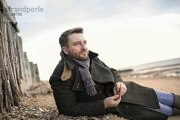 Gelassener Mann im Wintermantel entspannt am Strand