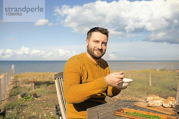 Porträt glücklich Mann Essen auf sonnigen Ozean Strand Terrasse