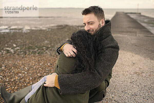 Glückliches Paar in Wintermäntel umarmen auf Ozean Steg