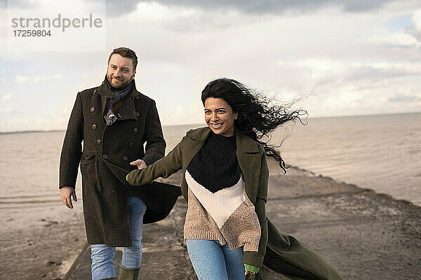 Glückliches Paar in Wintermänteln  die sich auf dem Bootssteg an den Händen halten