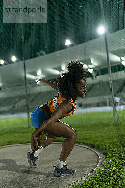 Weibliche Leichtathletin wirft Diskus im Stadion bei Nacht