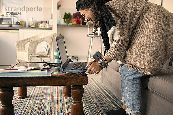 Glückliche Frau arbeitet von zu Hause am Laptop im Wohnzimmer