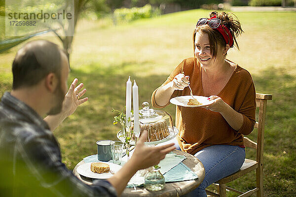 Glückliches Paar  das Kuchen und Tee am sonnigen Gartentisch genießt