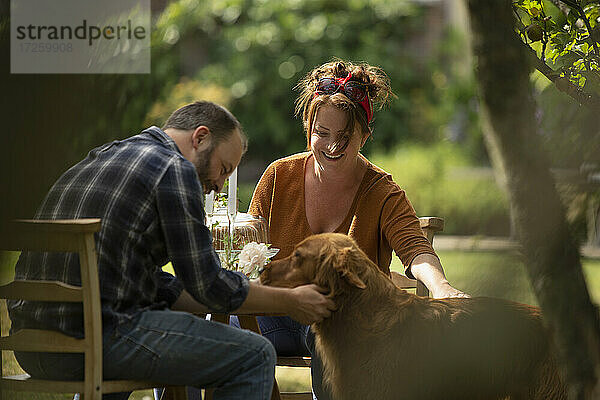 Glückliches Paar mit Golden Retriever Hund am Gartentisch