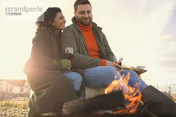 Glückliches Paar genießt Rotwein am Feuer am Winterstrand