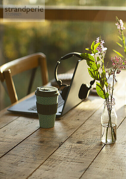 Laptop  Kaffee und einfacher Wildblumenstrauß auf Cafétisch