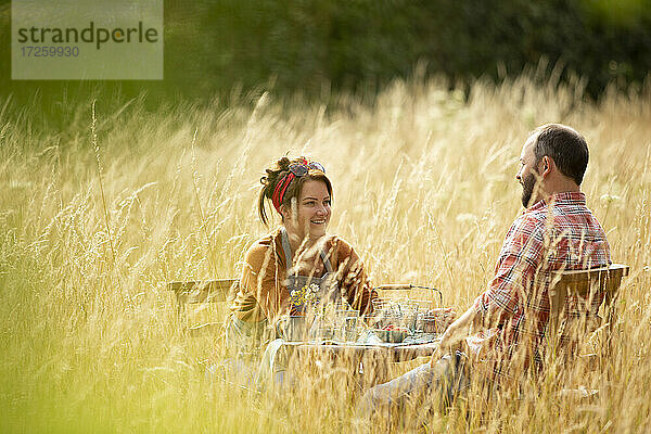 Glückliches Paar entspannt am Tisch im sonnigen hohen Gras