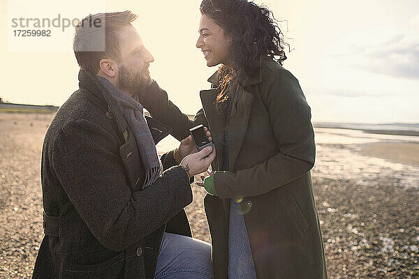 Freund mit Ehering macht seiner Freundin am Winterstrand einen Heiratsantrag