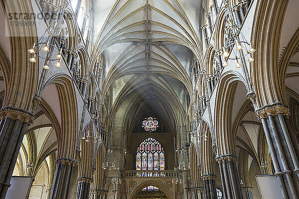 Blick entlang des sonnenbeschienenen Kirchenschiffs auf das farbenfrohe Buntglasfenster Great West Window der Kathedrale von Lincoln  Lincoln  Lincolnshire  England  Vereinigtes Königreich  Europa