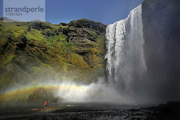 Wasserfall  Regenbogen  Tourist in roter Regenjacke  Skogafoss  Südisland  Island  Europa