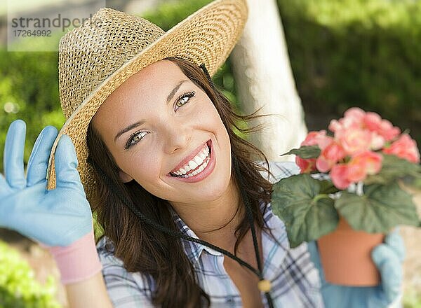Attraktive glückliche junge erwachsene Frau mit Hut bei der Gartenarbeit im Freien