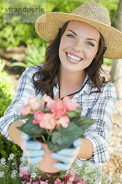 Attraktive glückliche junge erwachsene Frau mit Hut und Handschuhen bei der Gartenarbeit im Freien