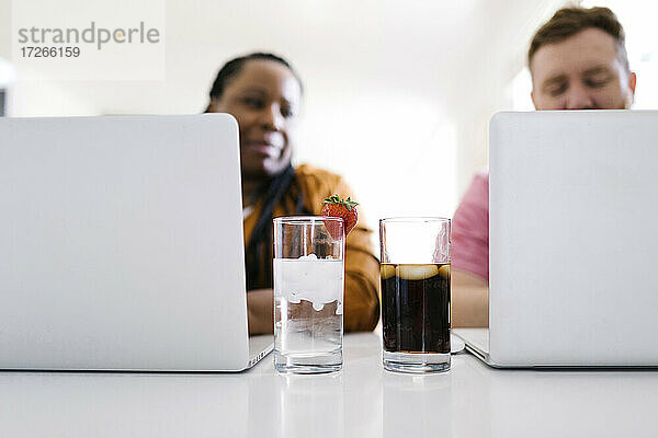 Wasser und Limonade in Gläsern zwischen Mann und Frau  die an Laptops arbeiten