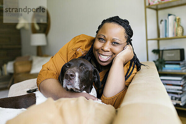 Lächelnde Frau umarmt Hund auf Sofa