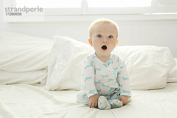 Baby Junge mit offenem Mund sitzt auf dem Bett
