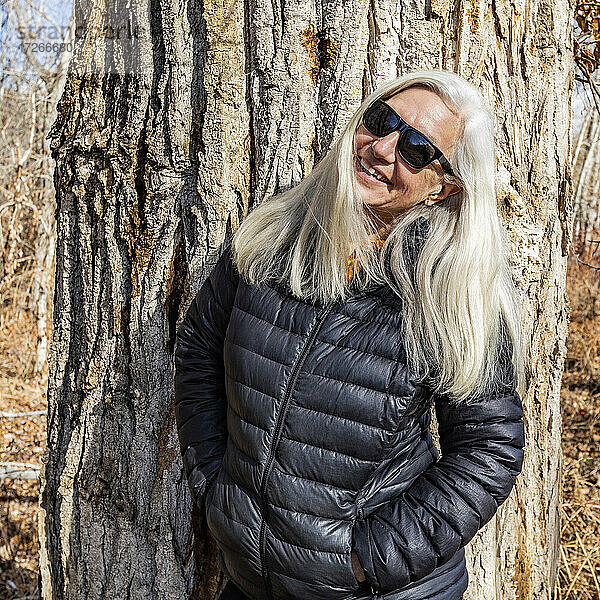 Porträt einer älteren Frau  die vor einem Pappelbaum steht