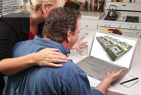 Ehepaar in der Küche mit Laptop mit Stapeln von Geld auf dem Bildschirm