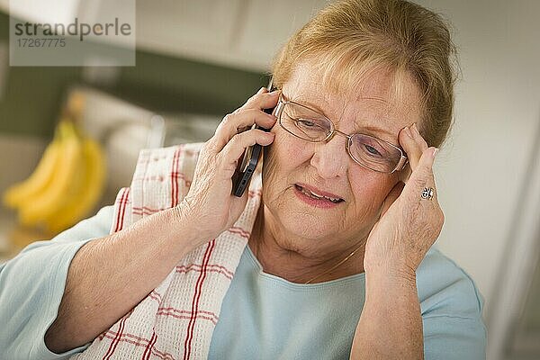 Geschockte ältere Frau am Handy in der Küche