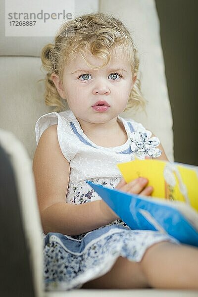 Adorable blondhaarige blaue Augen kleines Mädchen lesen ihr Buch auf dem Stuhl