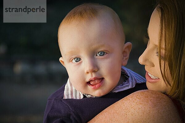 Adorable roten Kopf Säugling Junge Porträt mit seiner Mutter im Freien in dramatischen Beleuchtung