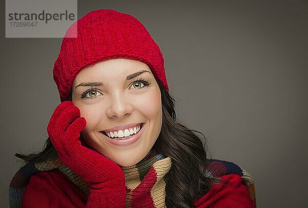 Glückliche gemischtrassige Frau mit Wintermütze und Handschuhen auf grauem Hintergrund