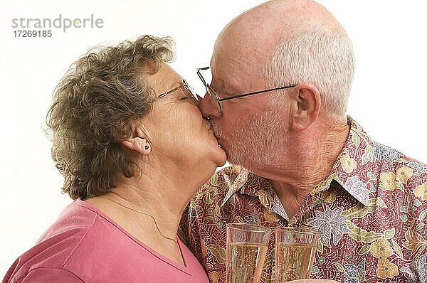 Glückliches älteres Paar  das sich mit Champagnergläsern küsst  vor einem weißen Hintergrund