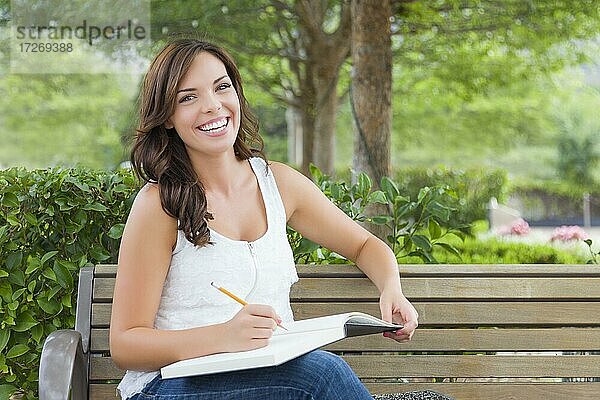 Attraktive junge erwachsene Studentin auf Bank im Freien mit Büchern und Bleistift