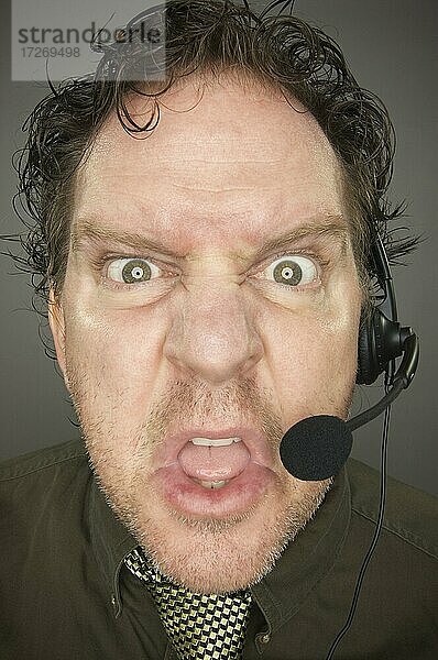 Irate Geschäftsmann trägt ein Telefon-Headset gegen einen grauen Hintergrund