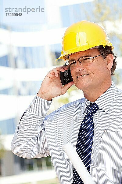Gutaussehender Bauunternehmer mit Schutzhelm und Krawatte lächelt  während er in sein Handy spricht